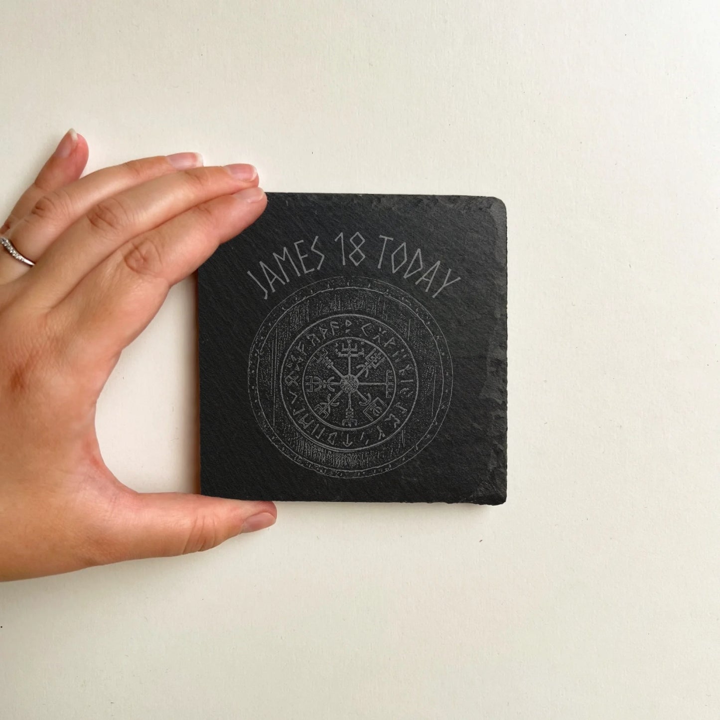Blank square black slate coaster held in hand for scale on a white background, natural hand-cut edges, 100 mm square (4 in).