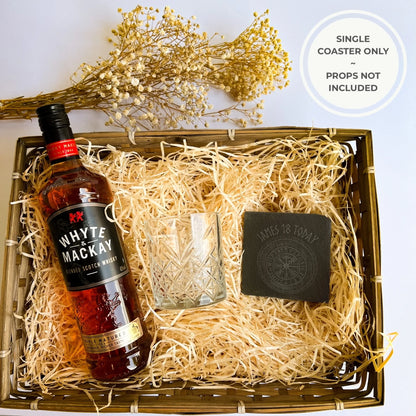 slate coaster gift Square black slate coaster in a wicker hamper beside a cut-glass tumbler and whisky bottle, natural hand-cut edges, 10 cm square (4 in).