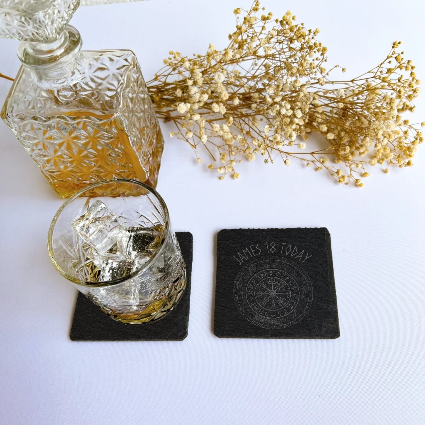 Two square black drinks mat coaster—one under a whisky tumbler to show scale, one blank to show engraving area, 10 cm square (4 in).