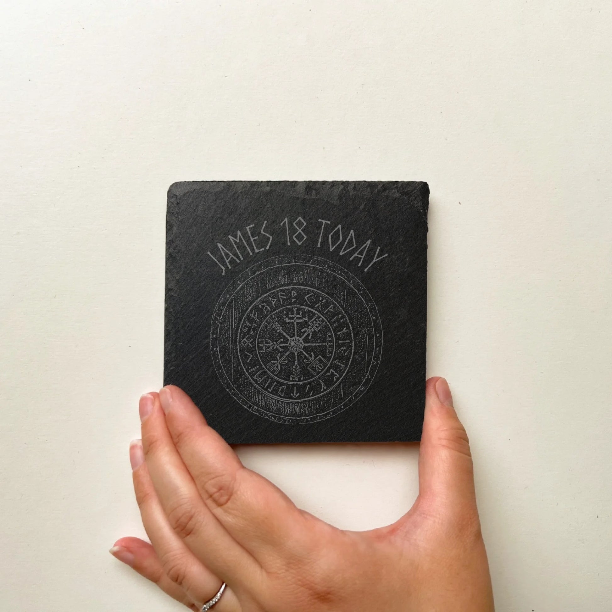 vegvisir Viking square black slate coaster held in hand for scale, natural hand-cut edges, 10 cm square (4 in).