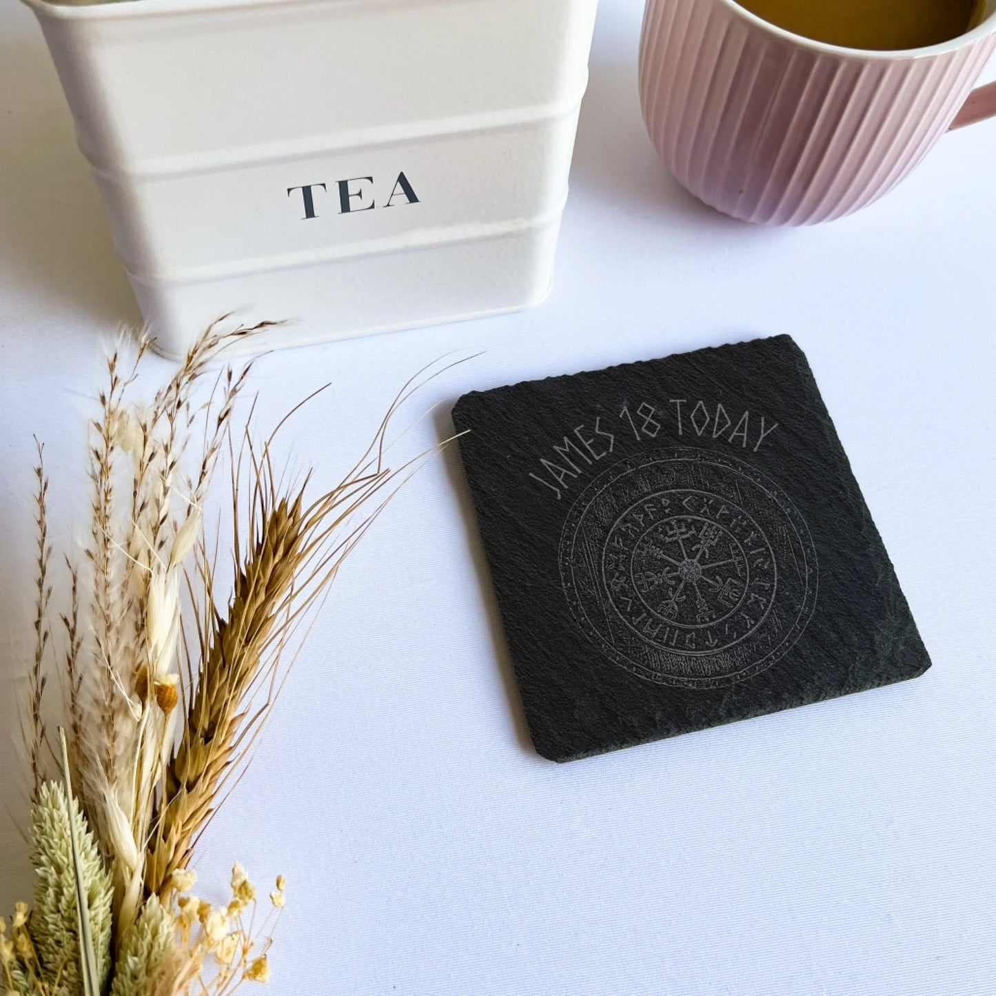 viking rune name Square black slate coaster beside a tea canister and pink mug, natural hand-cut edges, 10 cm square (4 in).