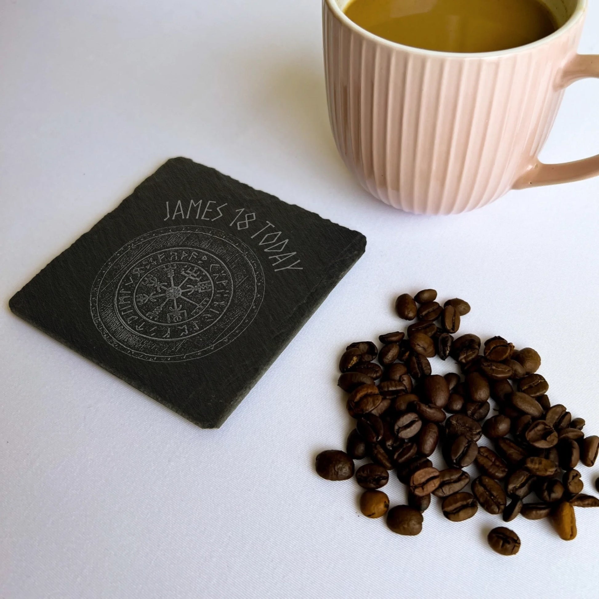 Blank square black slate coaster beside a pink mug and coffee beans, natural hand-cut edges, 10 cm square (4 in).