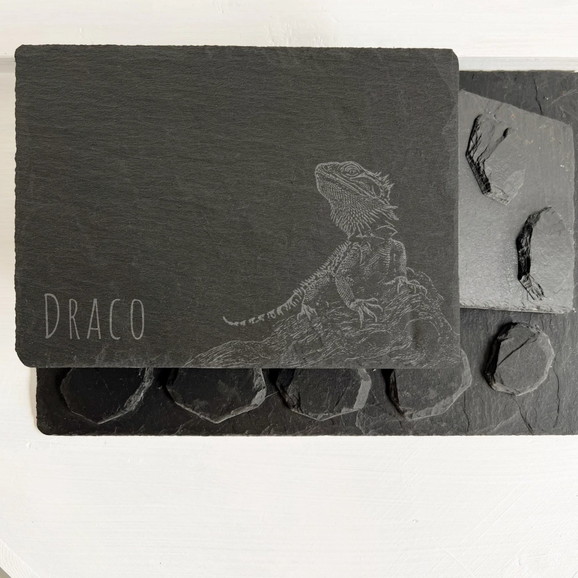 Bearded dragon Overhead view of rectangular black slate reptile hides and round slate pieces on a white surface.